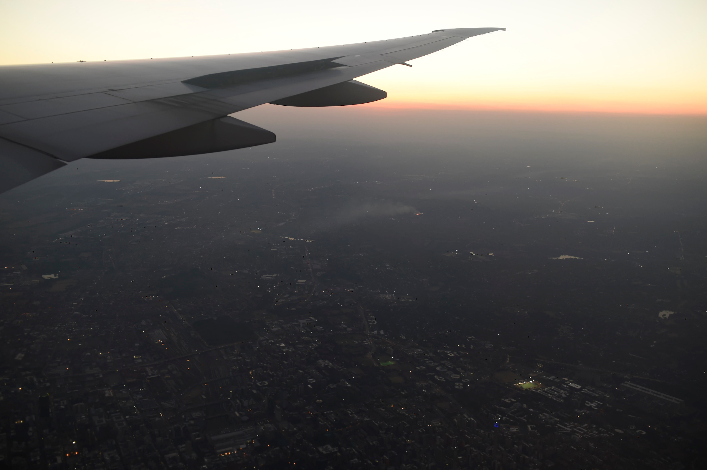 Photograph taken from inside an airplane showing the back of the right wing of the airplane and a city in the far distance below.